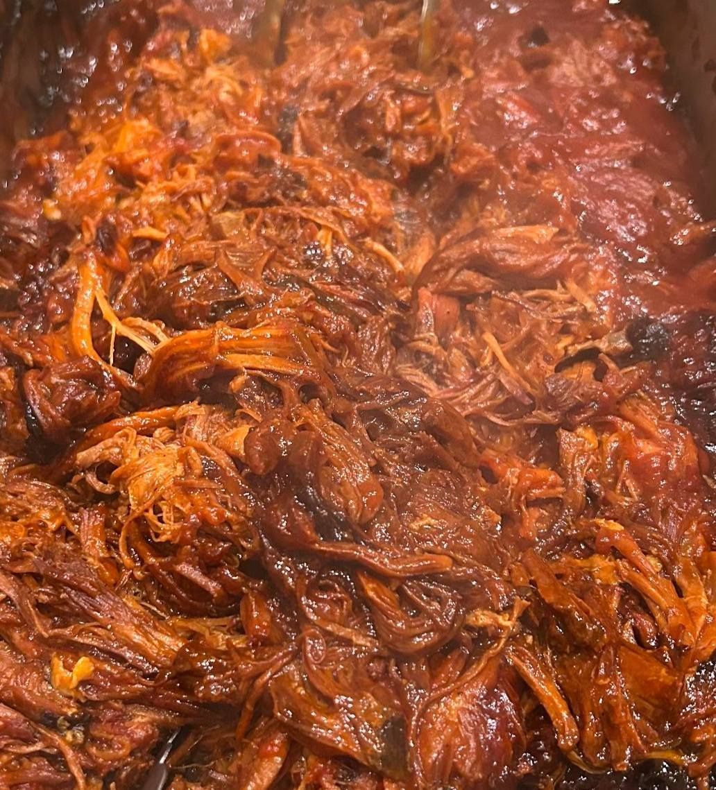 A close up of a pot of pulled pork in a sauce.