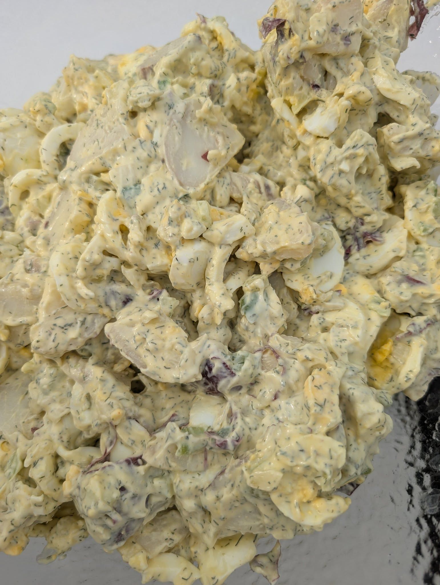 A close up of a potato salad in a bowl with a spatula.