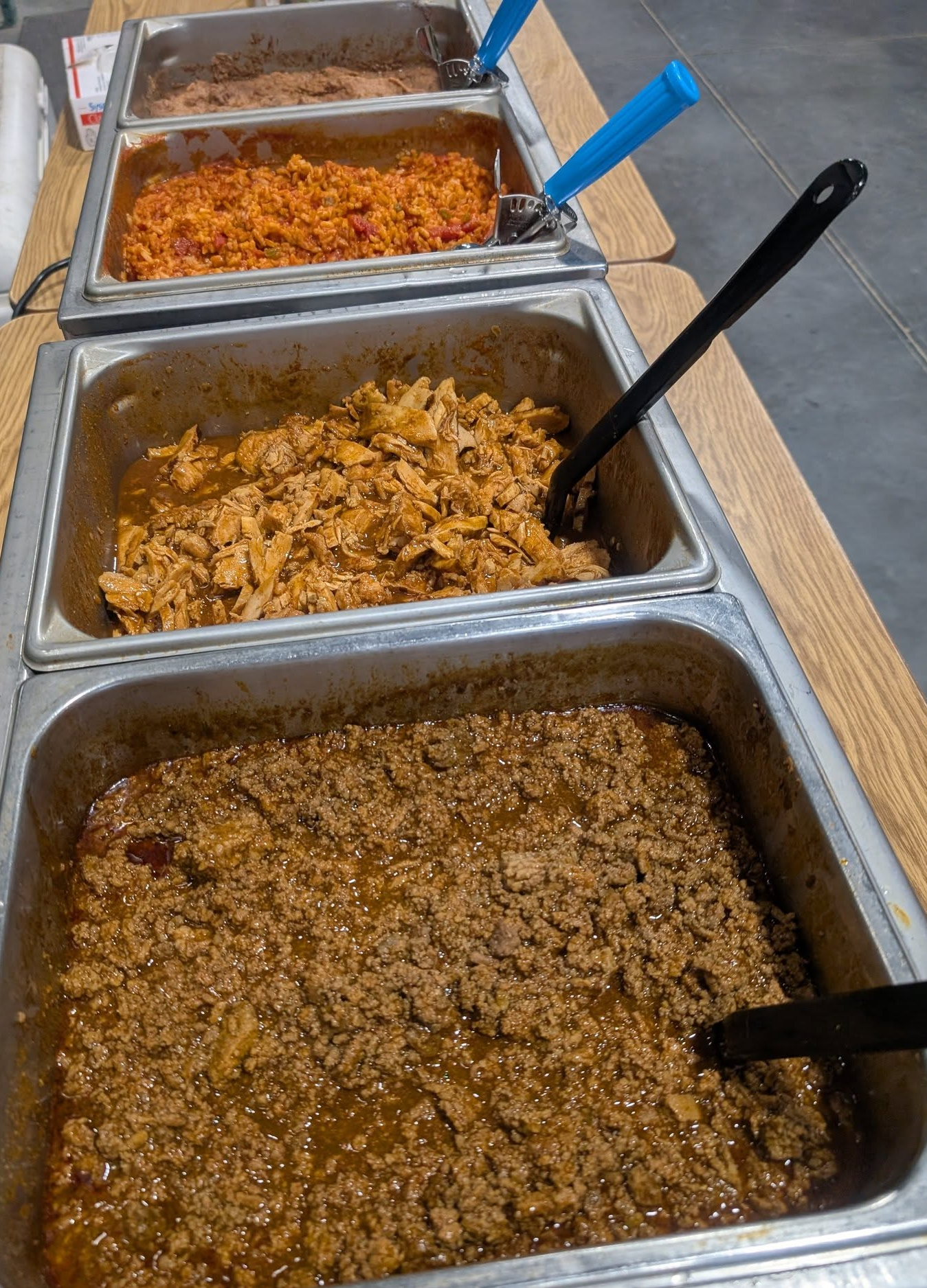 Three trays of food with spoons in them are on a table.