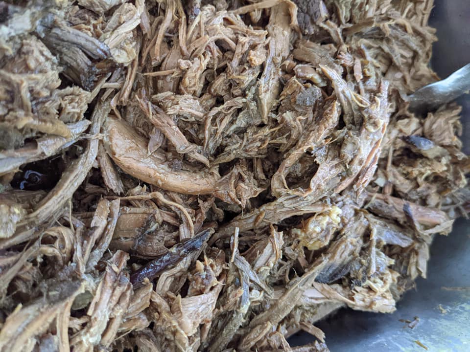A close up of shredded pork in a bowl with a spoon.
