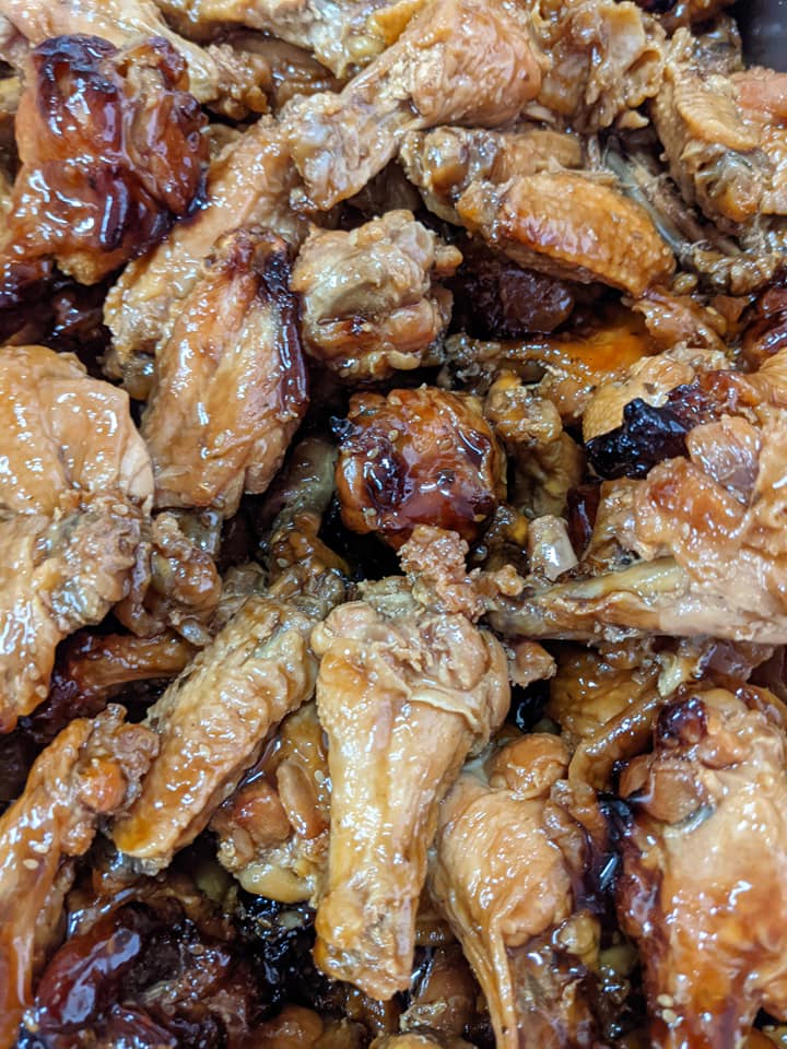 A close up of a pile of fried chicken wings covered in sauce.