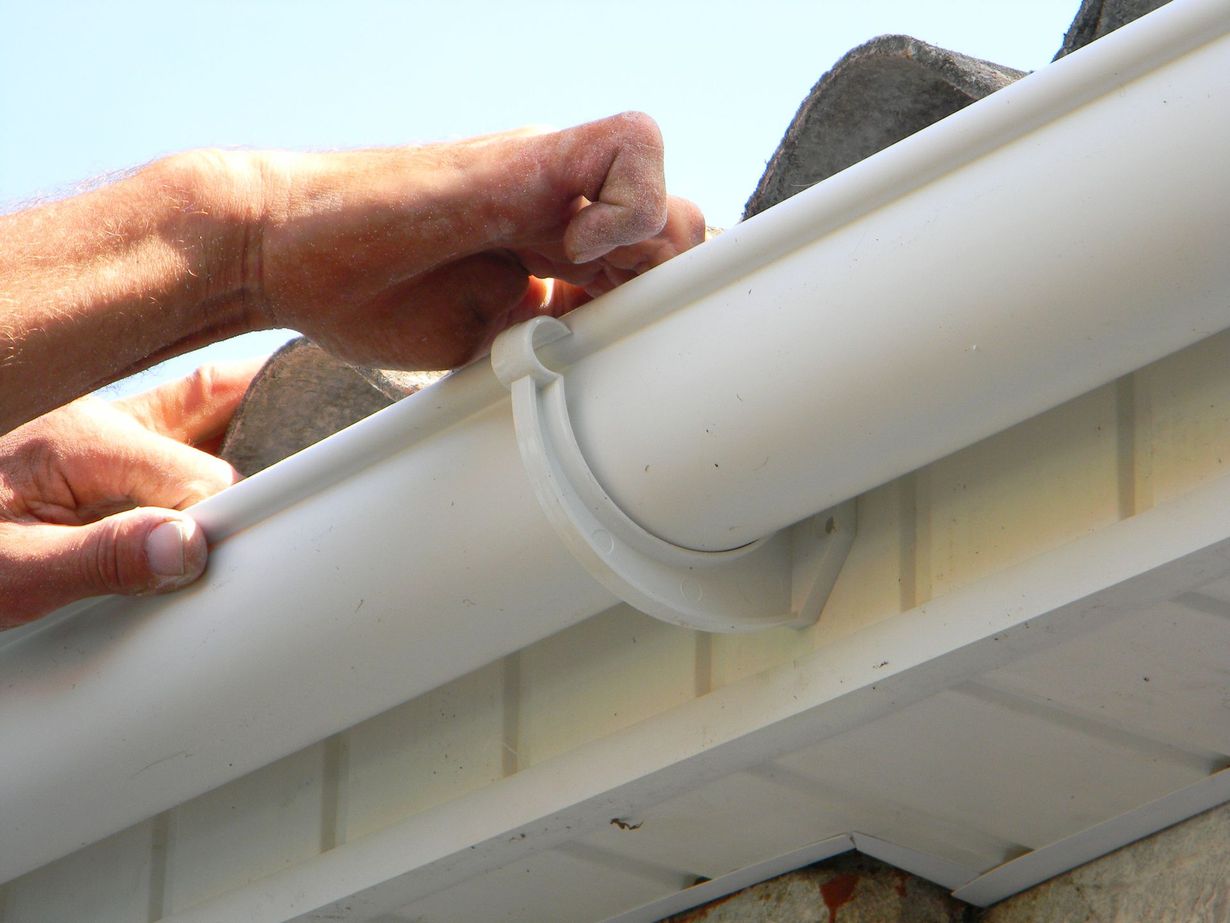 Hands attaching a white gutter pipe to a roof edge
