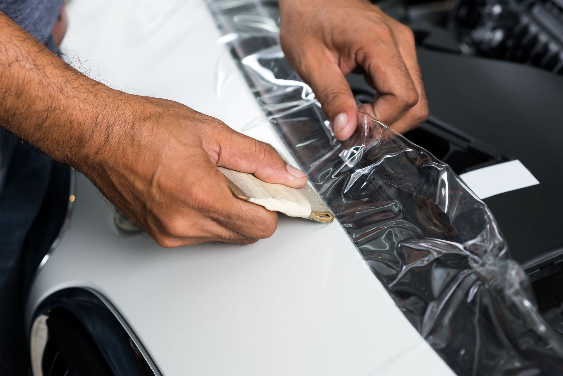 Hands applying masking tape to a white car panel during paint protection work