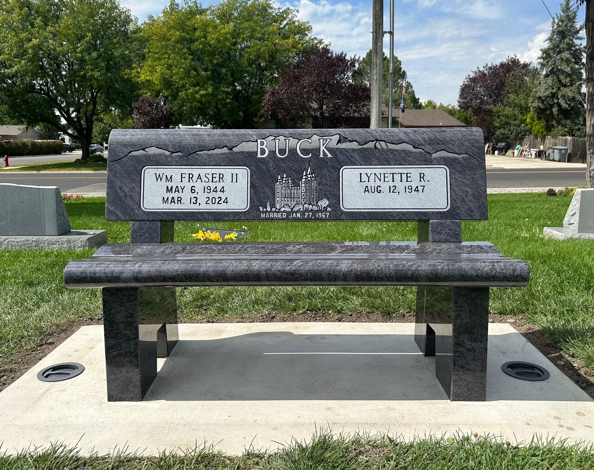 Granite memorial bench in a cemetery; engraved names and dates.