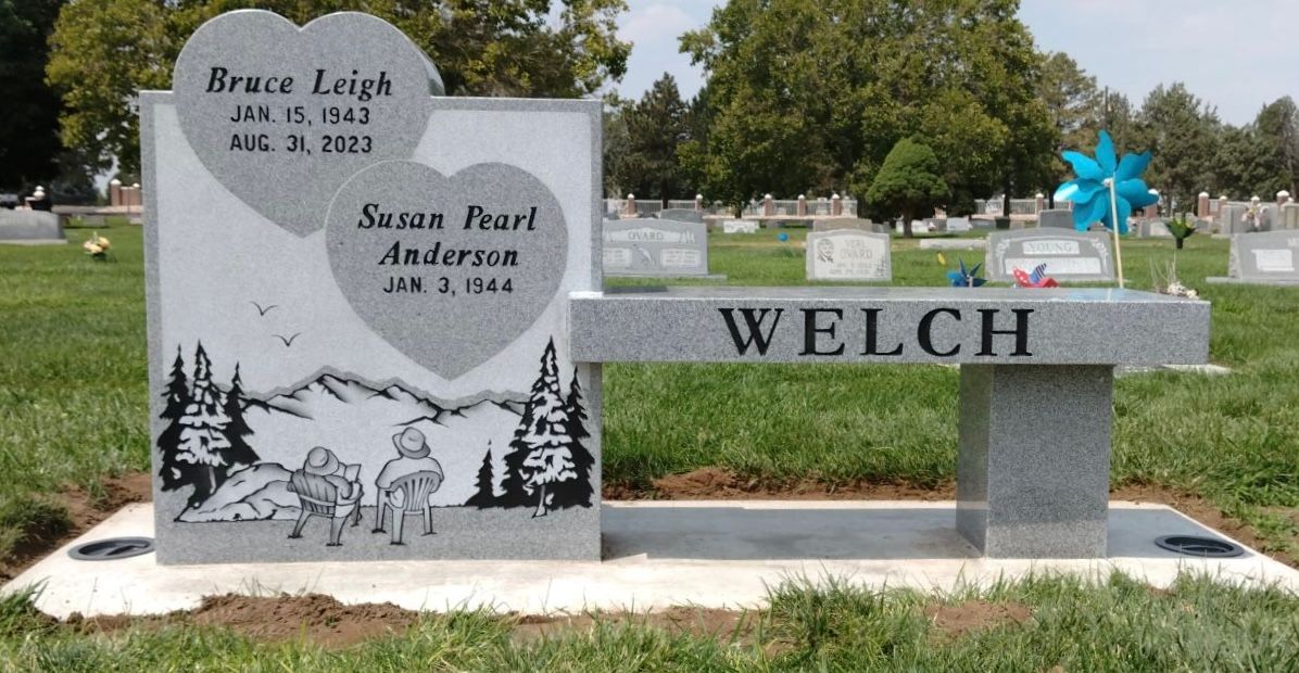 Monument with Welch name, heart-shaped inscriptions for Bruce Leigh and Susan Pearl Anderson, mountain scene, and bench.