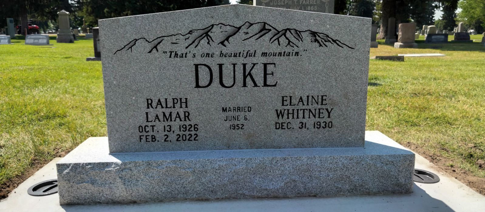 Gray granite headstone with the name Duke, names, and dates in a cemetery.