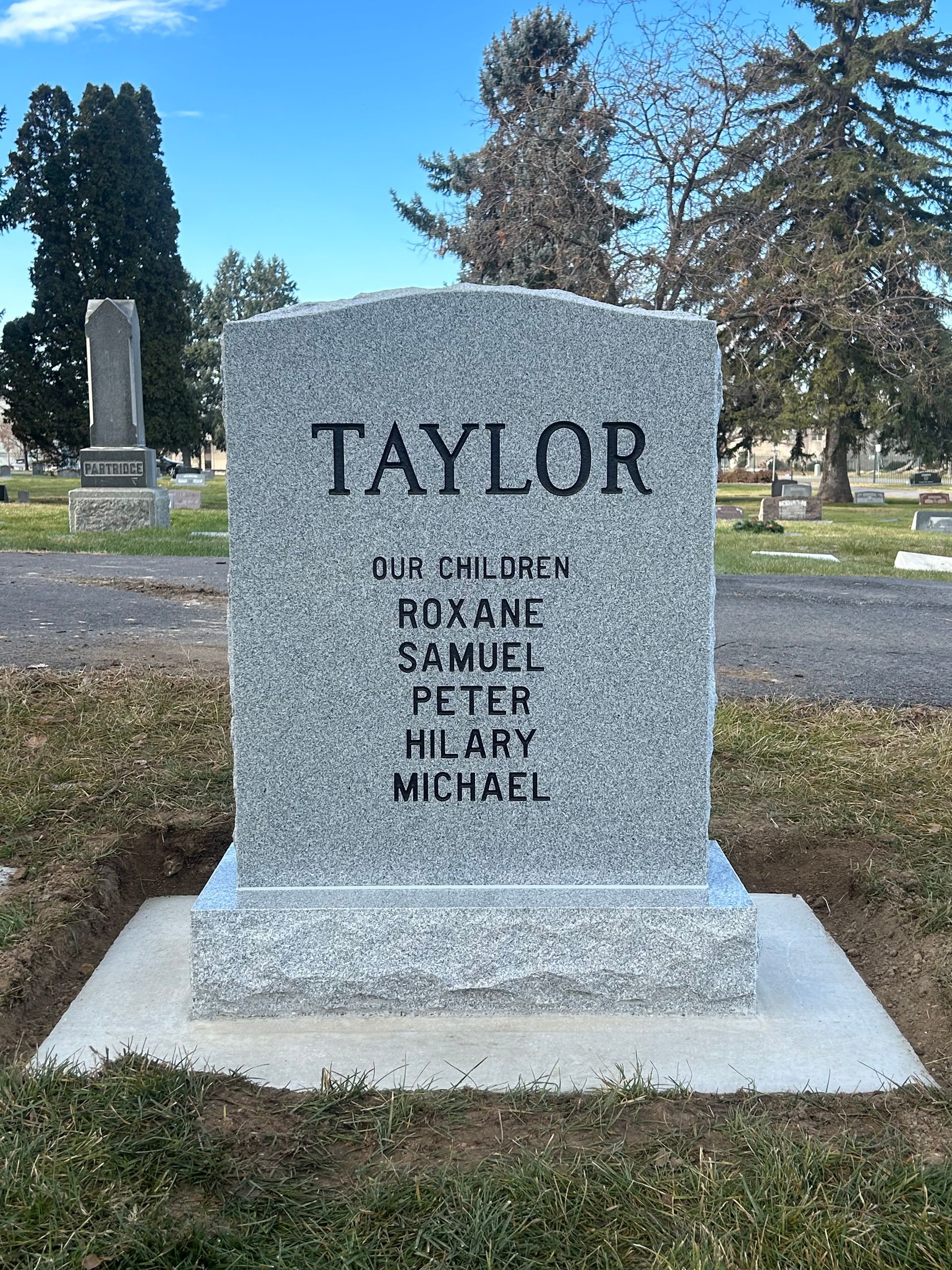 Headstone in a cemetery, inscribed with the last name Taylor and names of individuals below it.