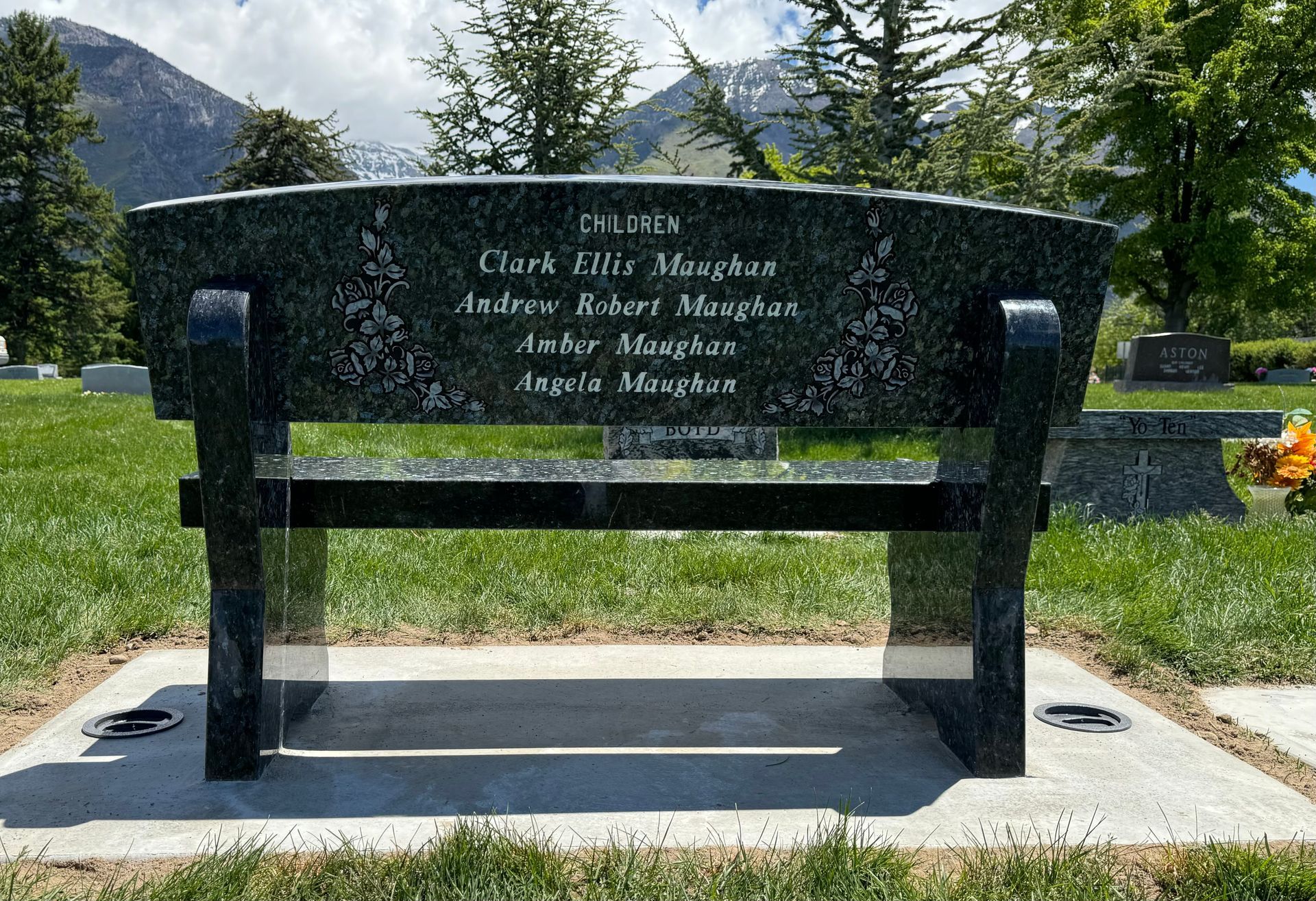 Black granite bench with engraved names in a cemetery. Mountains in background.