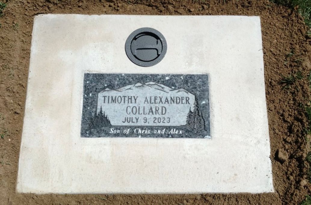 Headstone for Timothy Alexander Collard, with a mountain scene, in the ground.
