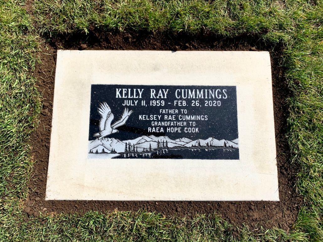 Gravestone of Kelly Ray Cummings, with name and dates, on a beige square within a patch of grass.