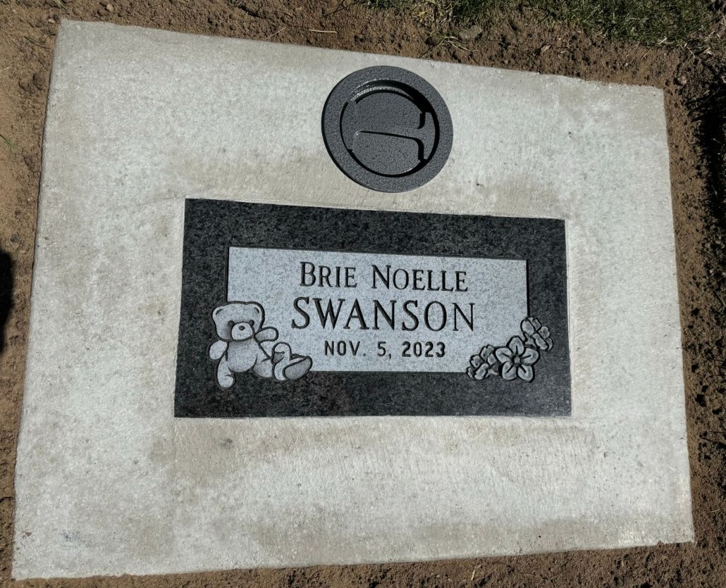 Headstone for Brie Noelle Swanson, with teddy bear and flowers, inscription Nov 5, 2023, in ground.