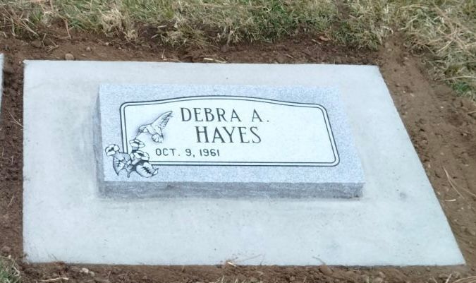 Headstone of Debra A. Hayes, born Oct. 9, 1961, on a concrete slab, with a floral design.