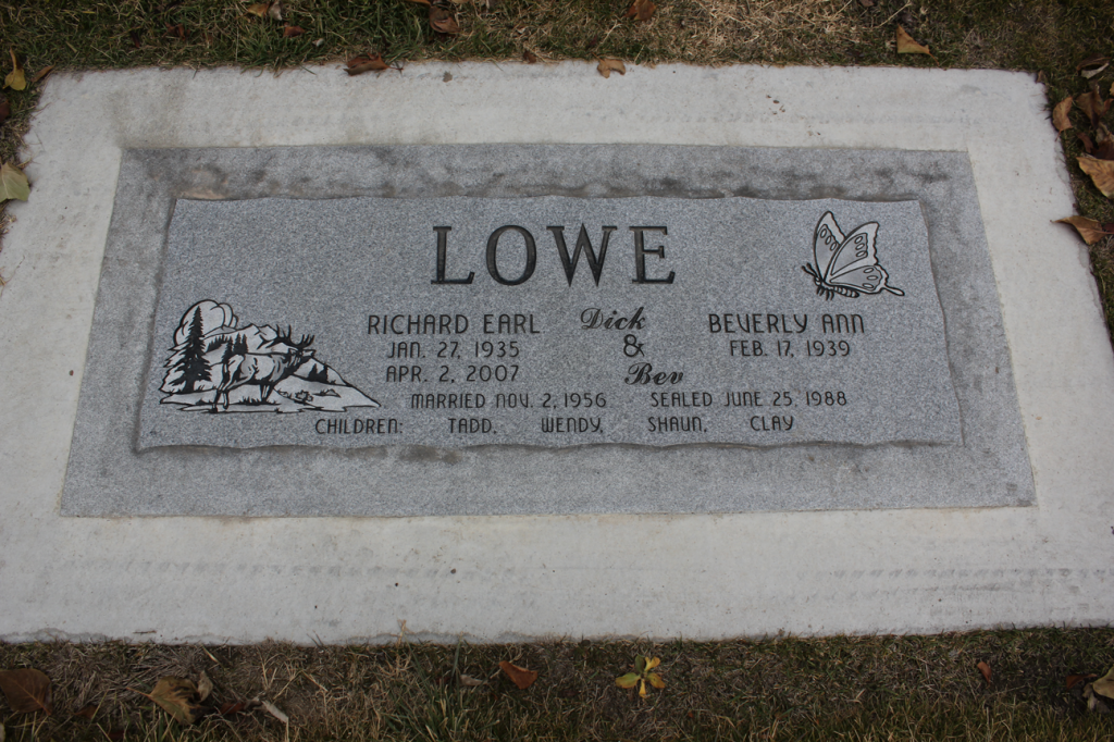 Gravestone engraved with the surname LOWE and names, dates, and decorative images of mountains and a crest.