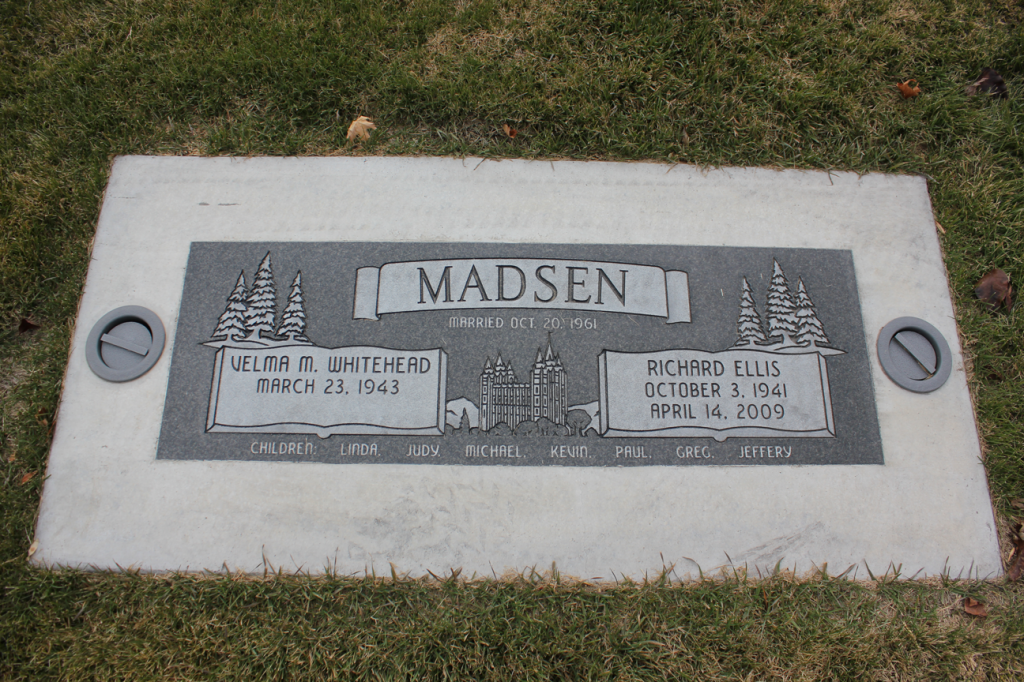 Gray headstone for Madsen family with dates and a banner, set in grass.