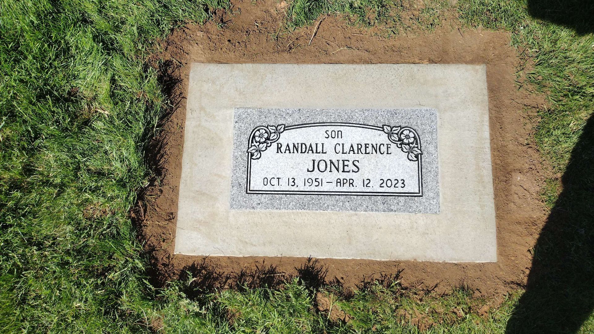 Tombstone for Randall Clarence Jones, surrounded by grass and dirt. Dates: Oct. 16, 1955 - Feb. 12, 2021.