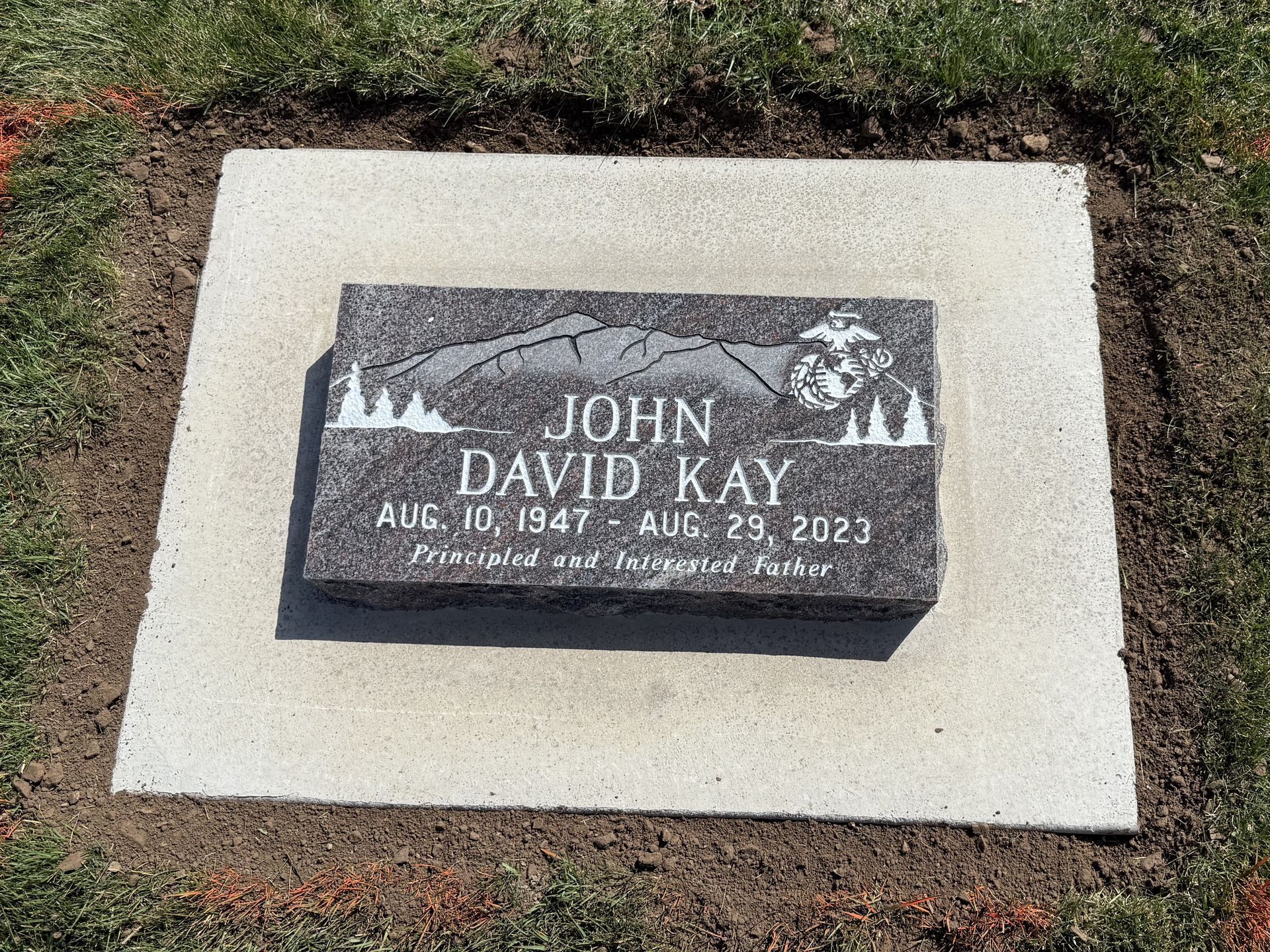 Grave marker for John David Kay, featuring mountain scene, dates Aug. 10, 1947 - Aug. 29, 2023, set on a concrete base.