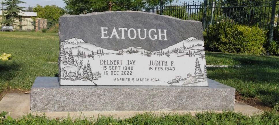 A grave marker with the name EATOUGH, with names, dates, and a desert scene etched into the stone.