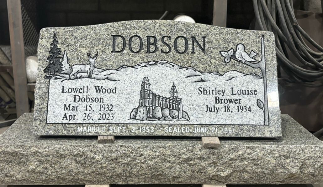 Granite headstone with the name Dobson, dates, and etched scenery.