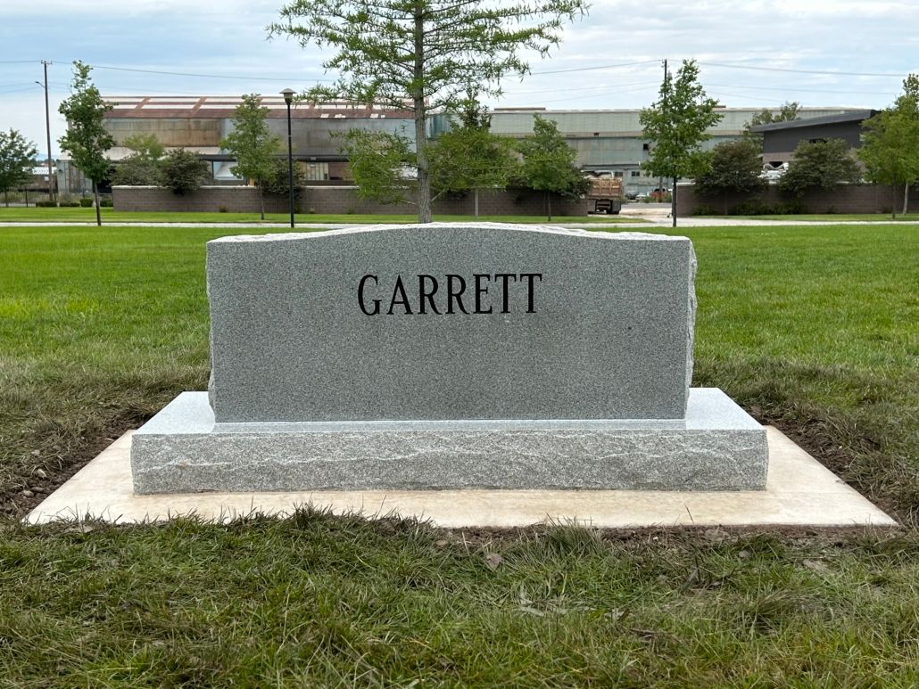 Gray tombstone in a grassy cemetery, engraved with the name 