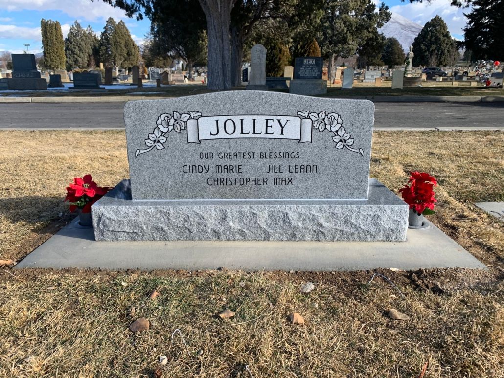 Grave marker of the Jolley family in a cemetery; grey stone with flowers in front.
