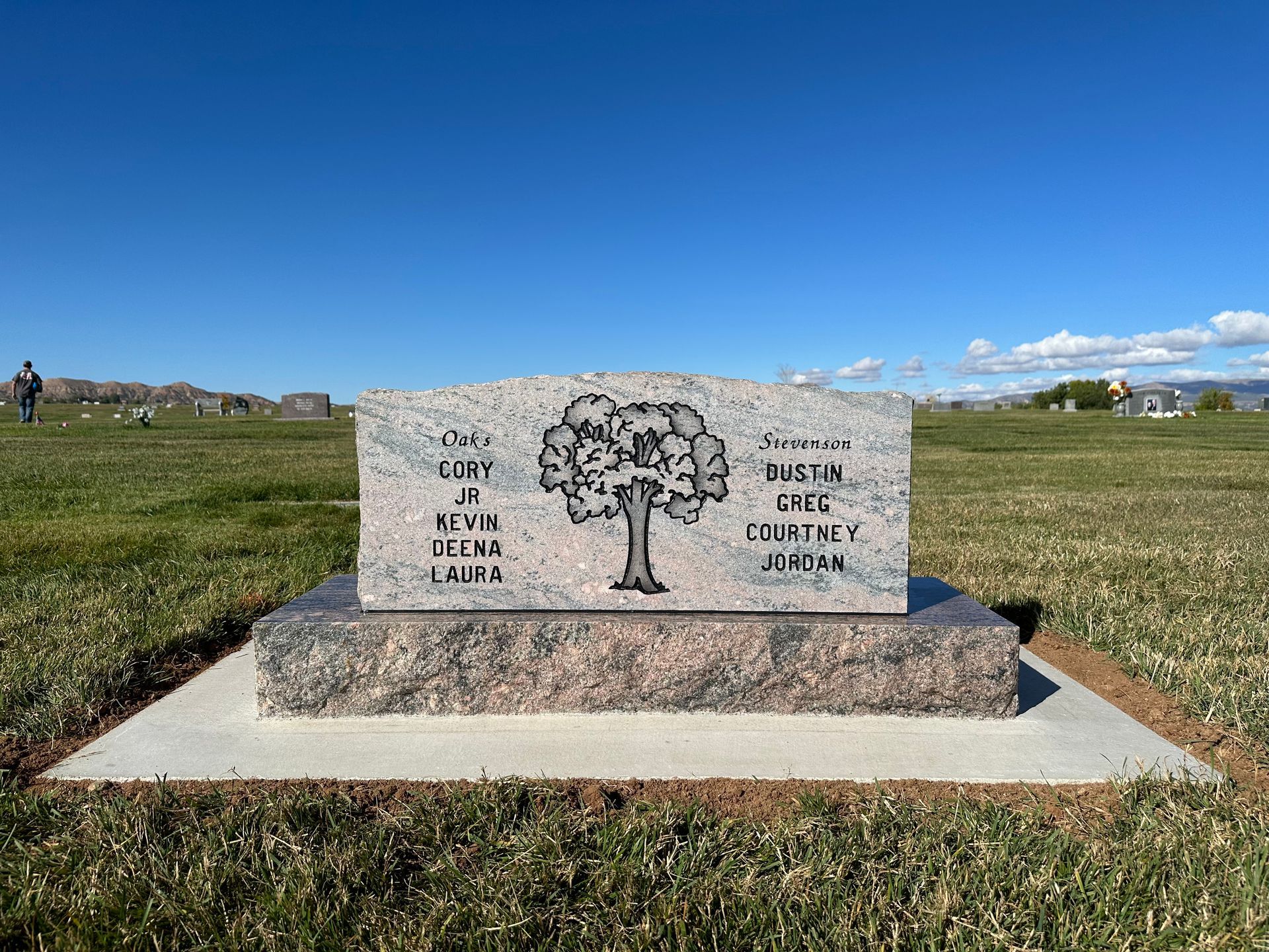 Headstone with tree design at a cemetery, blue sky in background.