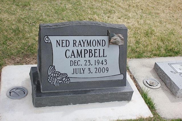Gray headstone with the name Ned Raymond Campbell, dates 1943-2009, in a grassy field.