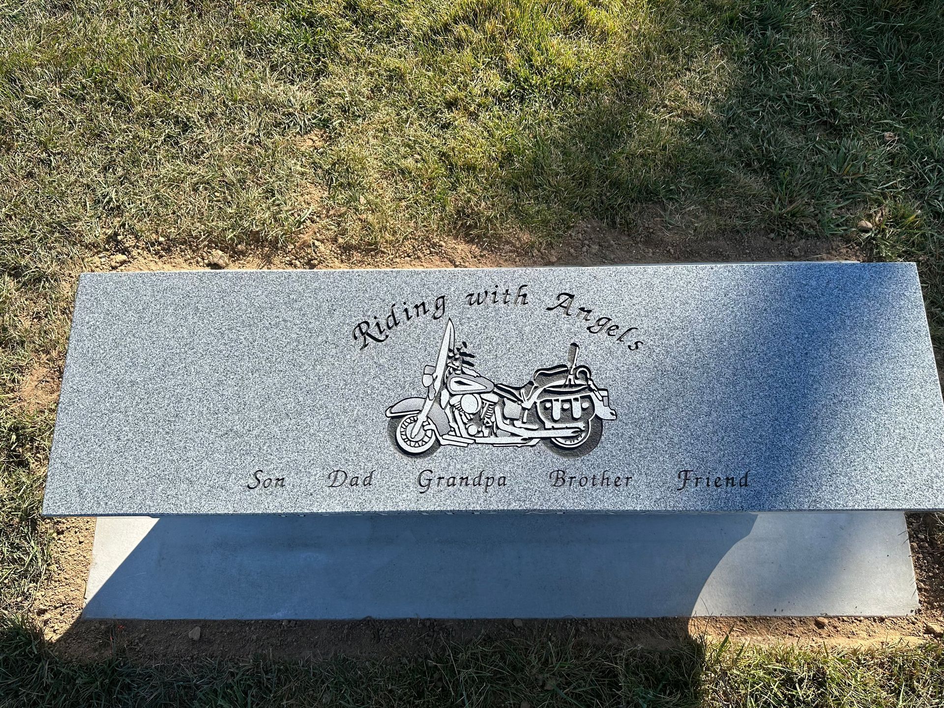 Gray granite bench with motorcycle engraving and Riding with Angels inscription; outdoors.