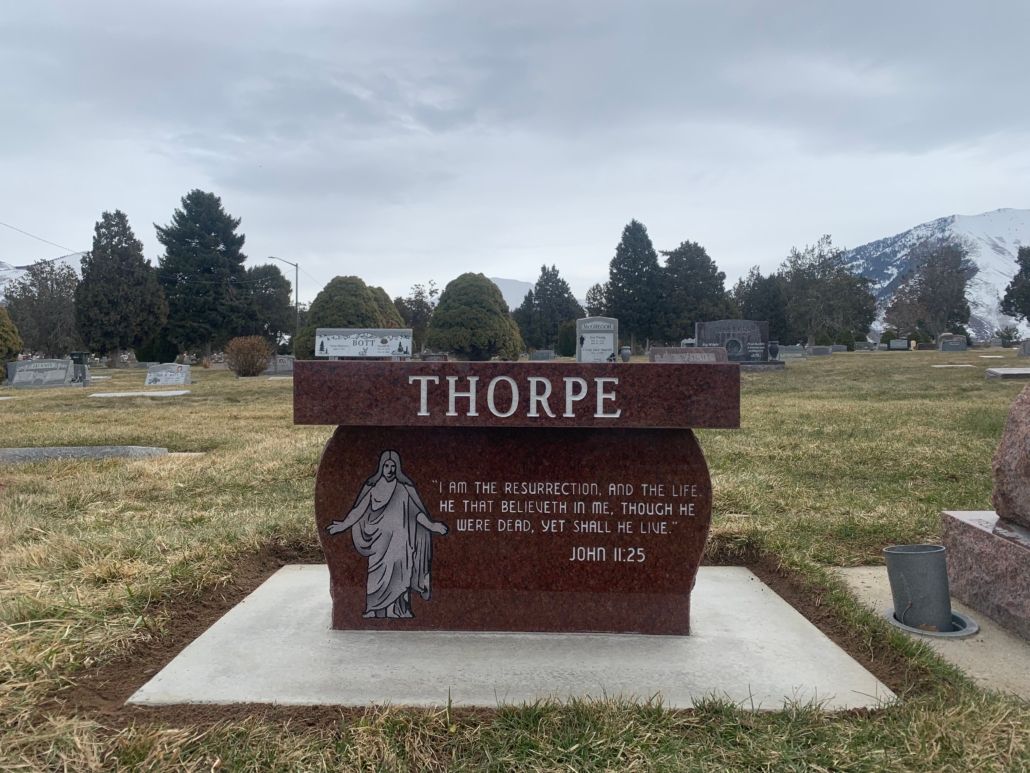 Red granite Thorpe headstone in a cemetery with snowy mountains in the background.