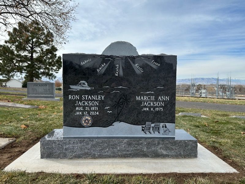 Black granite headstone with etched nautical scene, names Ron & Mardie Jackson.