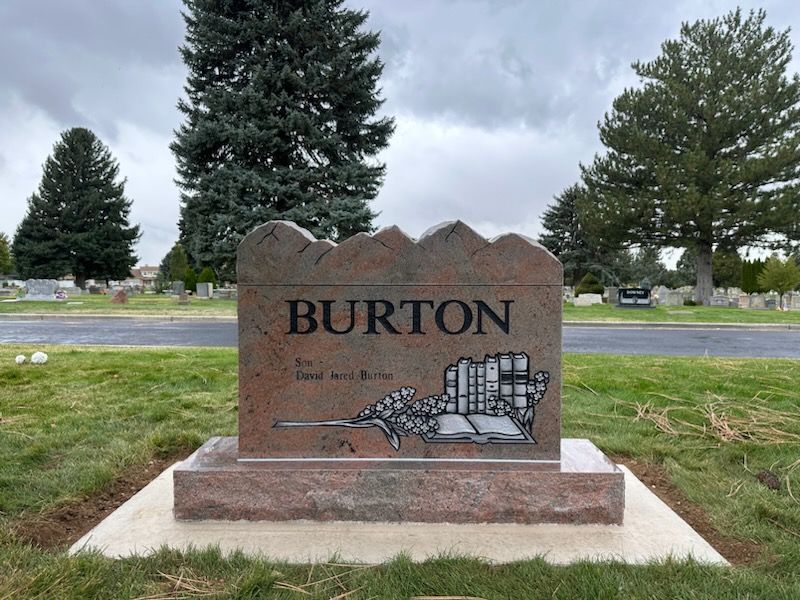 Red granite headstone with BURTON and etched drawing of books in a cemetery.