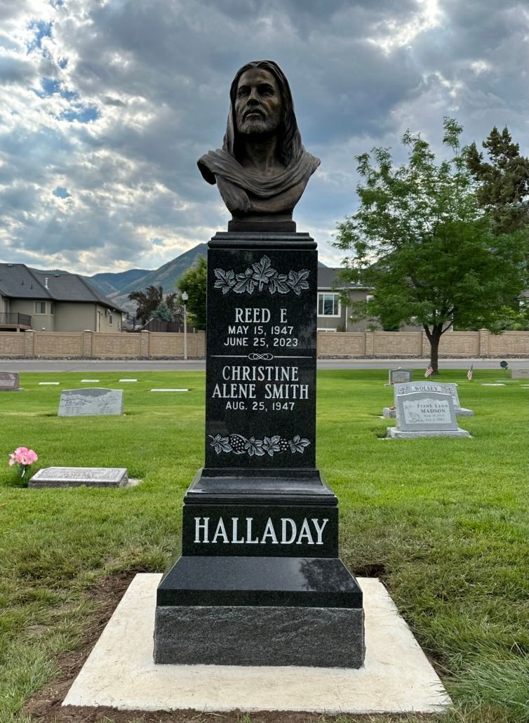 Headstone with bust of Jesus, in a cemetery, under a cloudy sky.