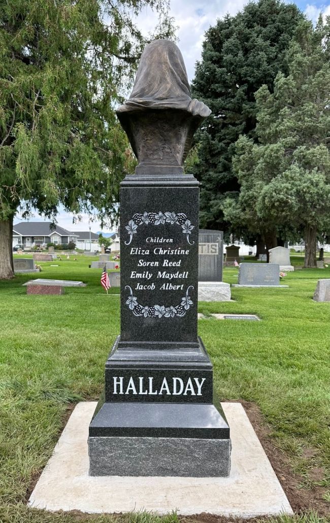 A tall, dark gravestone in a cemetery with the name Halladay and inscriptions.