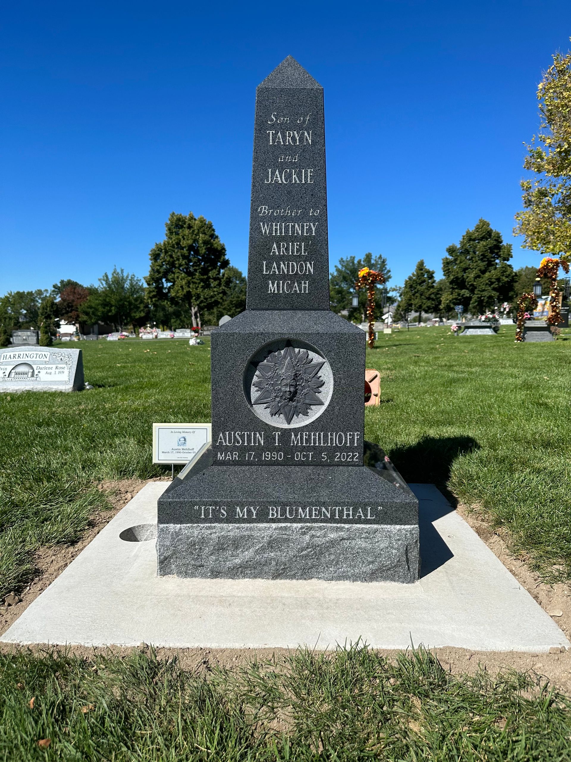 Tall granite tombstone in a cemetery with engraved names and a circular emblem.
