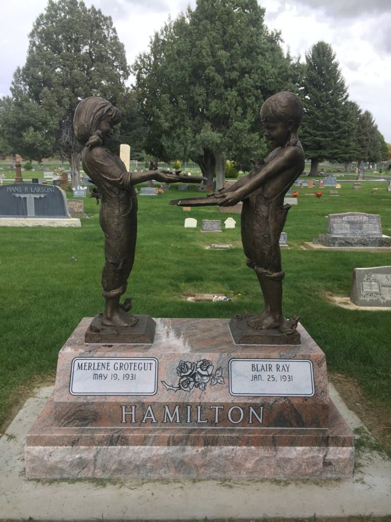 Bronze statues of two children, holding hands, on a grave marker in a cemetery