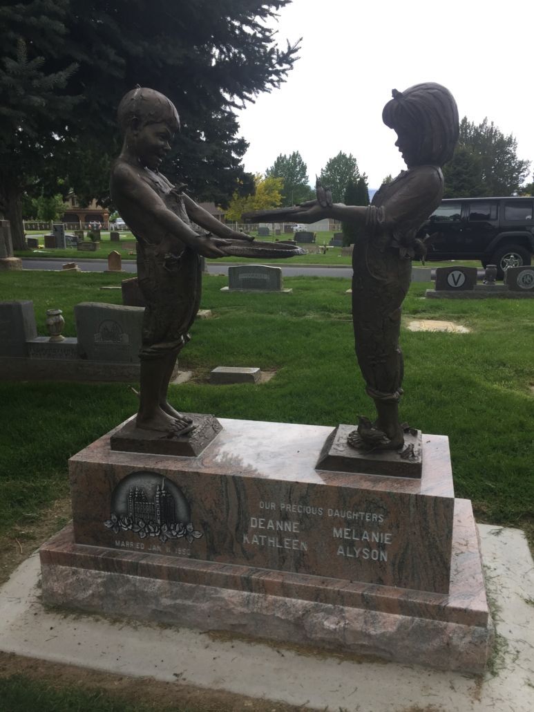 Bronze statues of children holding hands on a tombstone in a cemetery.
