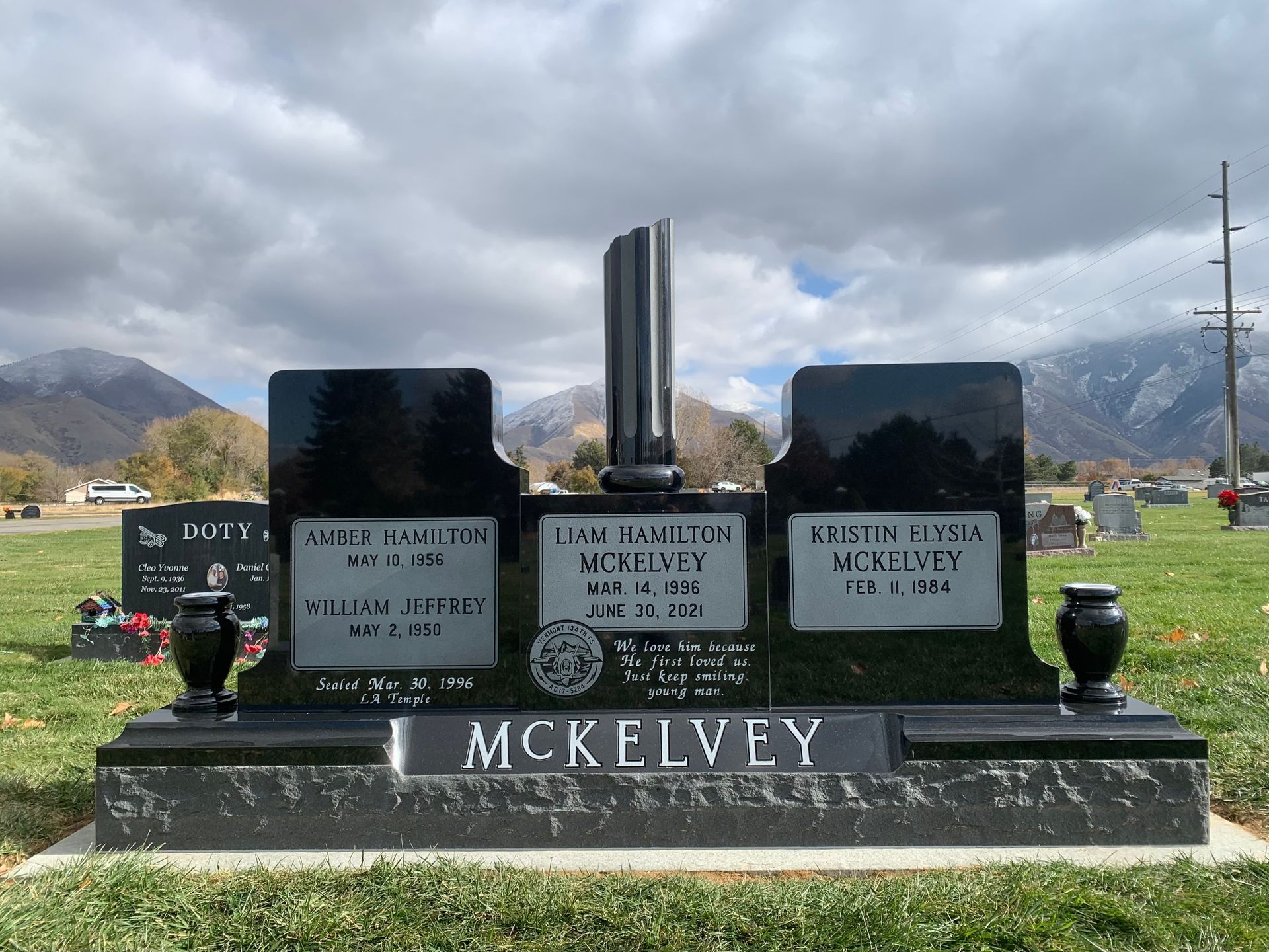 Black granite headstone for McKelvey family, with names and dates. Cemetery with mountains in the background.