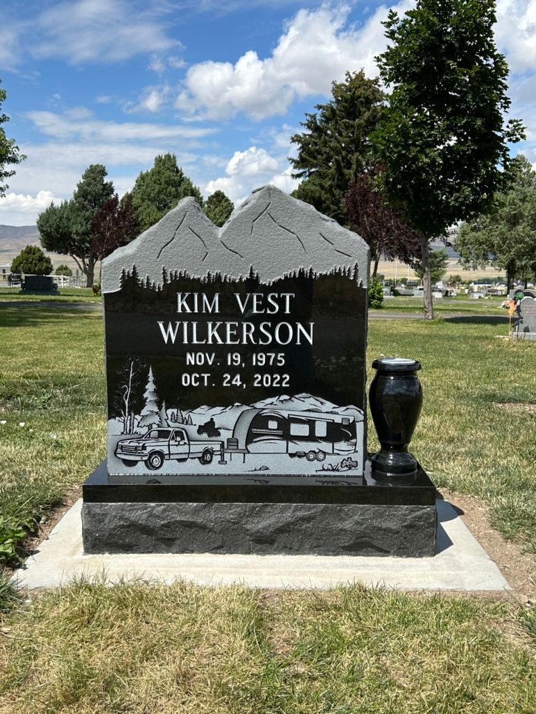 Black headstone with mountain top design, memorializing Kim Vest Wilkerson (1975-2022), with RV scene, at cemetery.