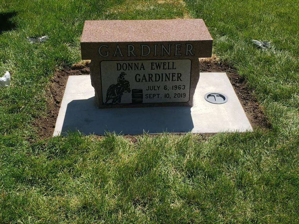 Headstone of Donna Ewell Gardiner, red-brown with white lettering and equestrian art on a rectangular stone base.