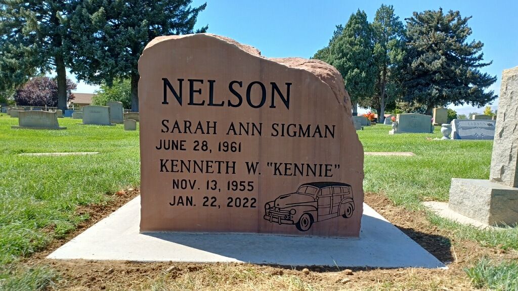 Headstone for the Nelson family in a cemetery. Includes names, dates, and a car graphic.