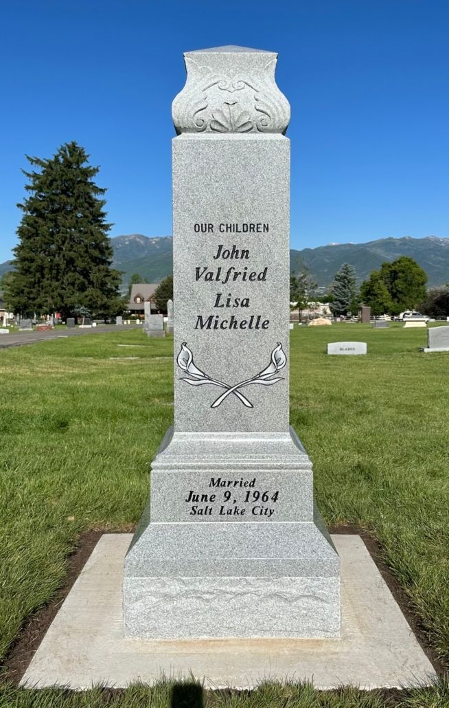 Tall gray headstone in a cemetery, inscribed with names, and date.