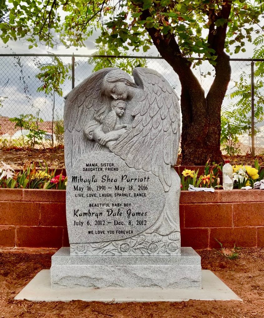 Stone angel statue gravestone with dates and names, in a cemetery.