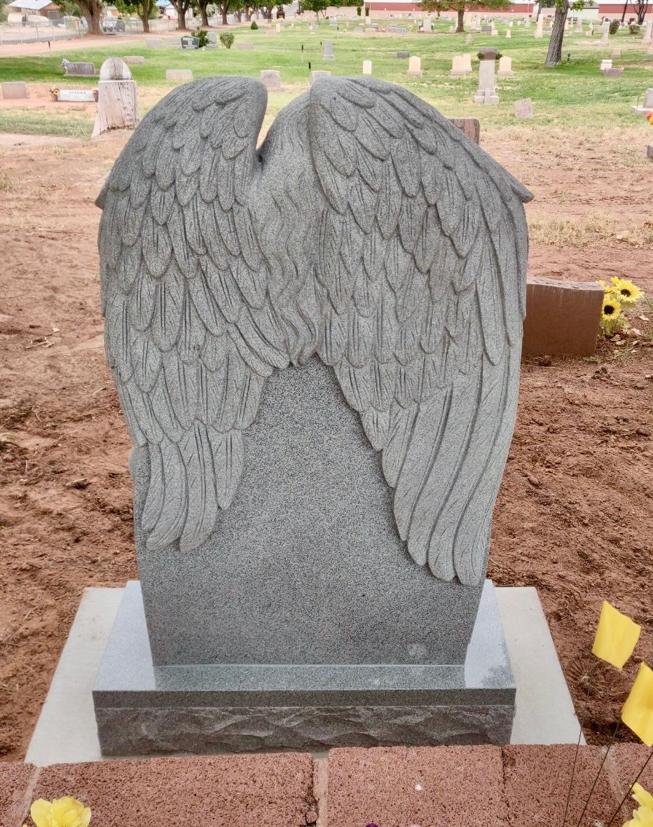 Gray angel wing headstone in a cemetery.