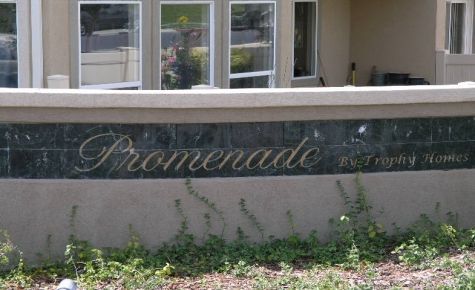 Sign for Promenade by Trophy Homes, with green vines at the base and windows in the background.