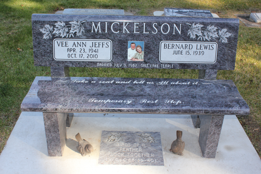 Granite bench headstone with names, dates, photo, and inscription in a cemetery.