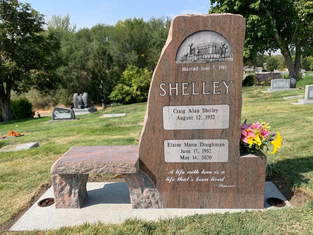 Headstone: Shelley with bench; dates and a small scene. Located in a cemetery with flowers.