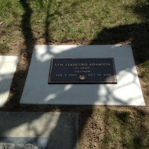 Grave marker for Lyn Stanford Adamson, US Army, Vietnam. Bronze plaque on a concrete slab in a grassy setting.