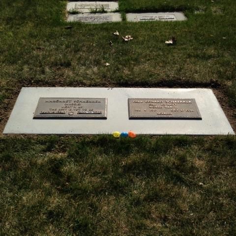 Grave with two nameplates on a flat stone, in green grass, with three small colored balls in front.
