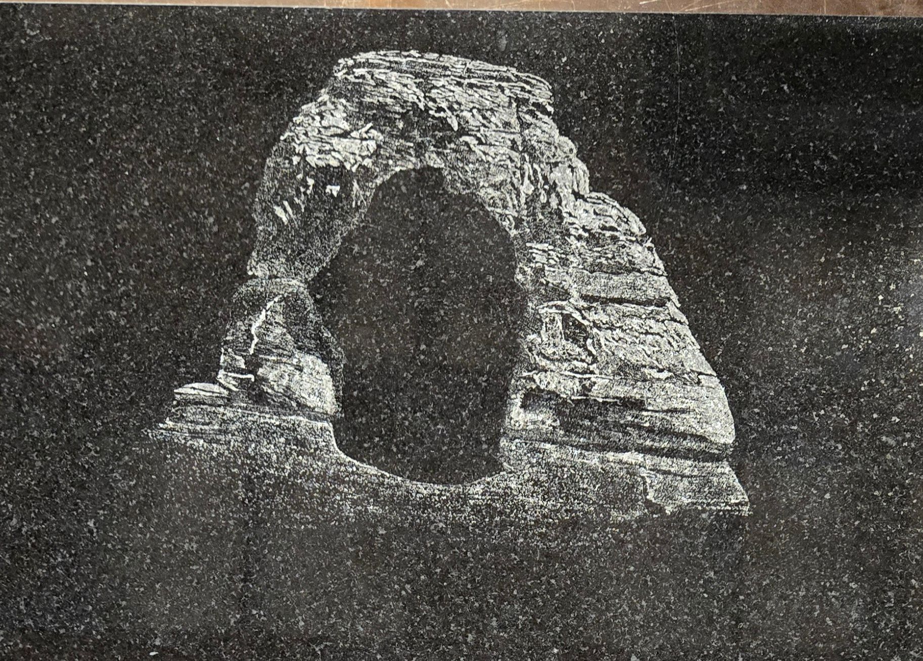 White etched image of Delicate Arch on a black speckled background.