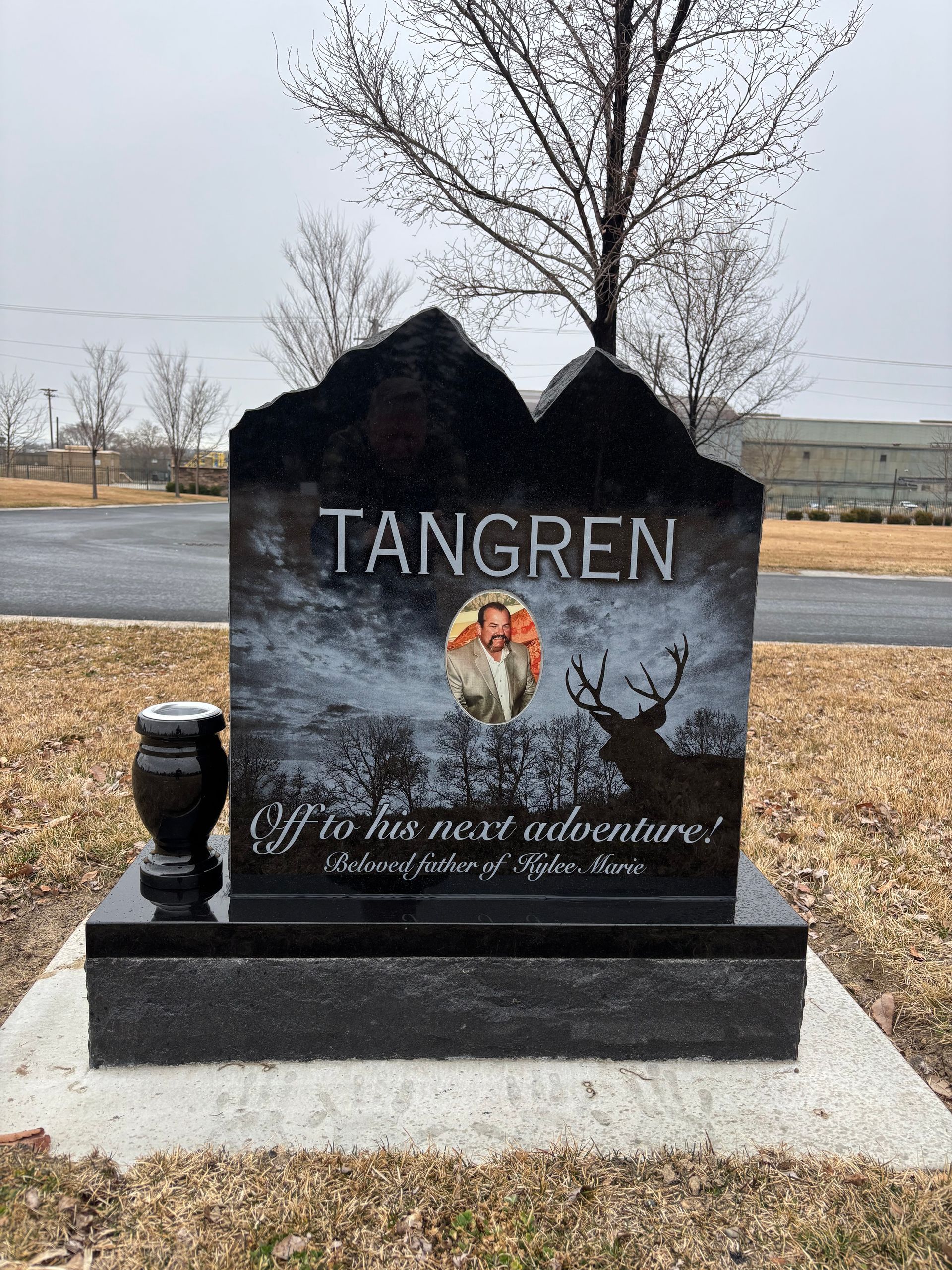 Black granite tombstone with Tangren inscription, mountain-shaped top, photo, deer silhouette, and Off to the next adventure!