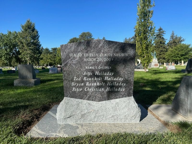 Grave marker in a cemetery. Gray stone lists family names: Halladay, with a blue sky and green grass.
